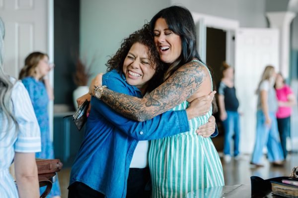 Two friends hugging and laughing in the cafe area of the Transformation Church lobby